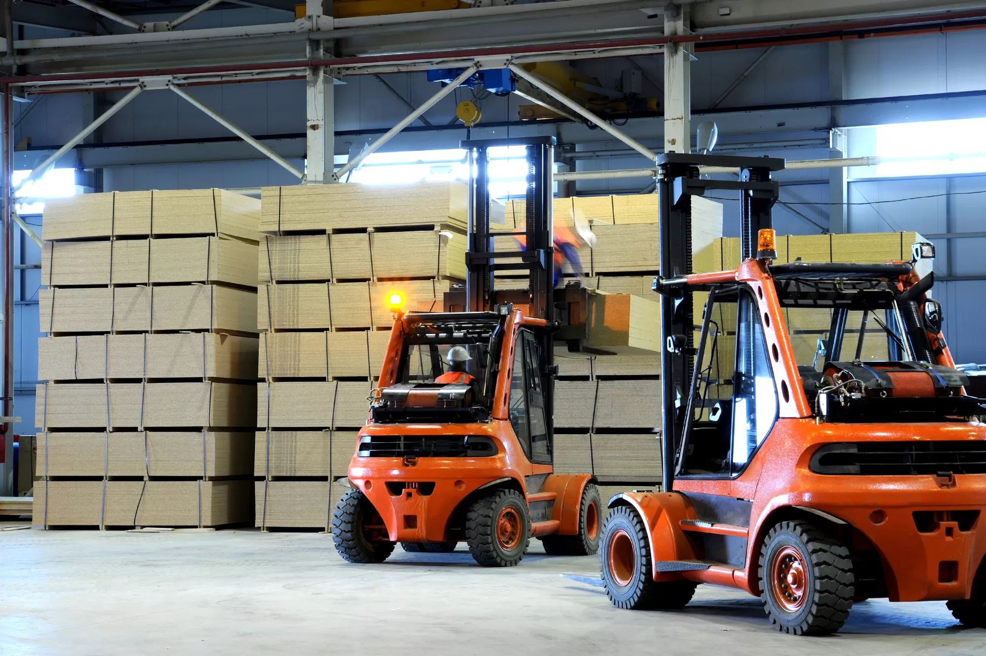 warehousing 2 forklifts lifting wooden slabs in warehouse